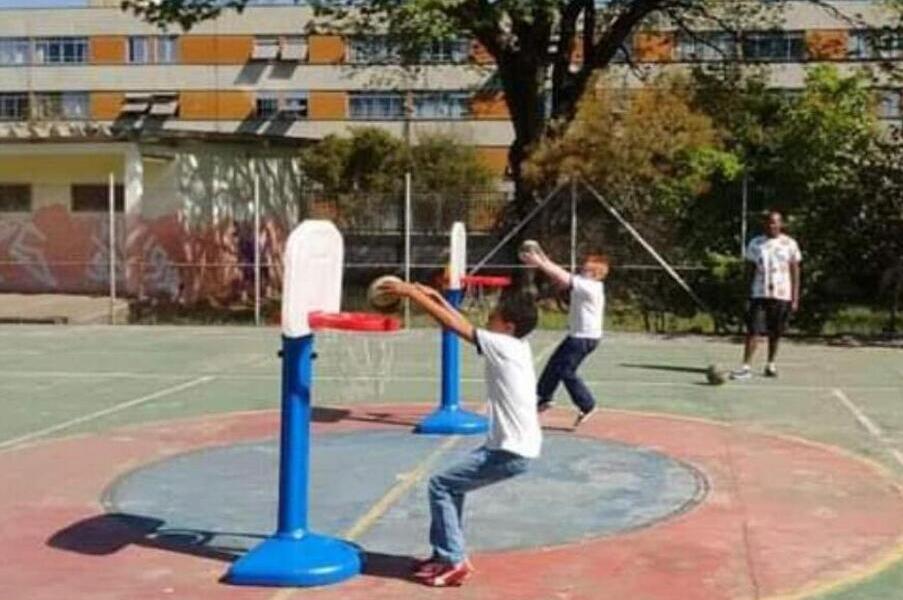 Crianças, em atividade física, brincam com a cesta de basquete