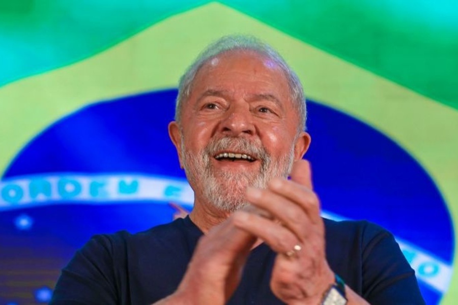 Lula sorri e aplaude. Atrás dele, uma enorme bandeira brasileira