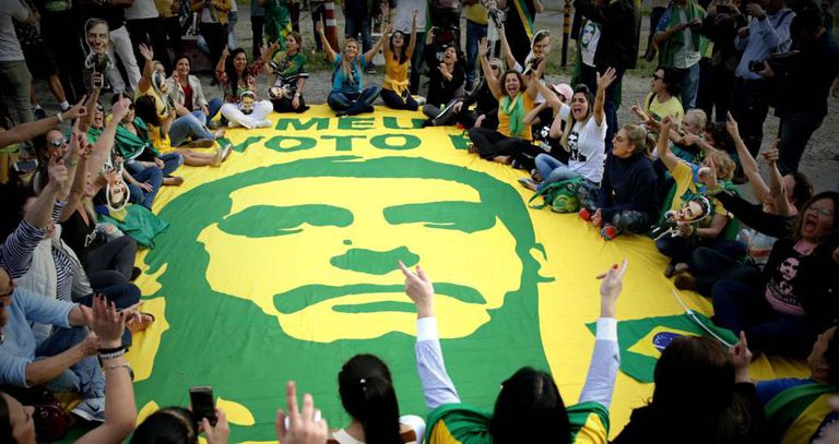 Foto de muita gente sentada em volta a uma imensa faixa com a foto de Bolsonaro