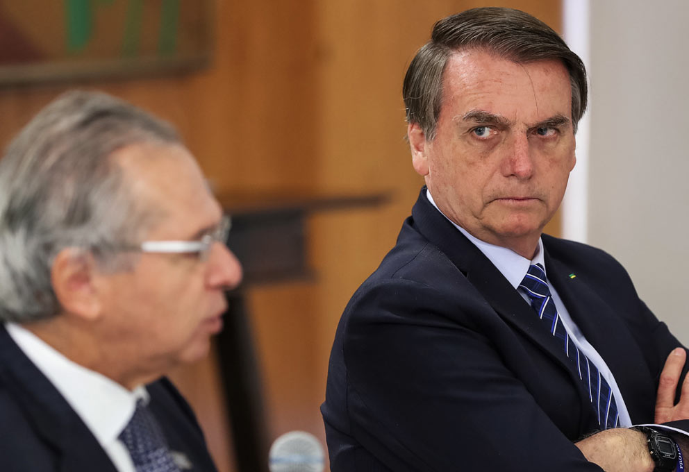 Foto de Bolsonaro de braços cruzados olhando feio para Paulo Guedes
