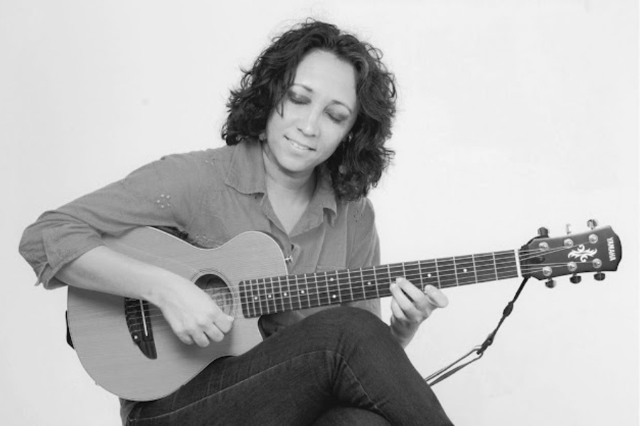 Foto de Socorro Lira sentada a um banco, tocando violão