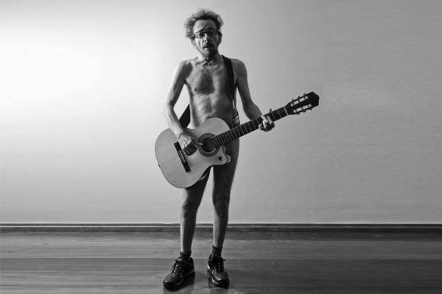 Foto do cantor e compositor Tom Zé nu com seu violão à frente. Veste apenas um tênis.