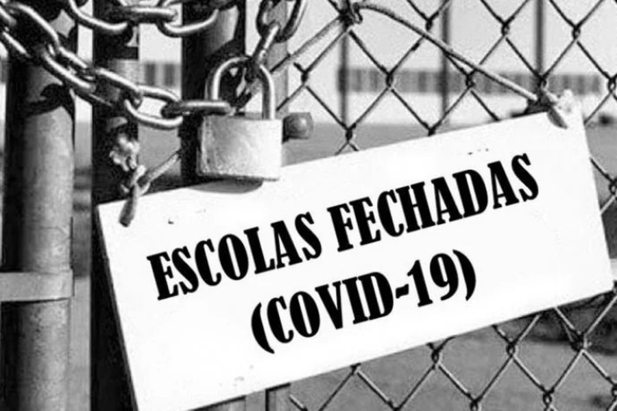 Cartaz colocado no portão de uma escola trancada a cadeado diz; Escolas Fechadas Covid-19