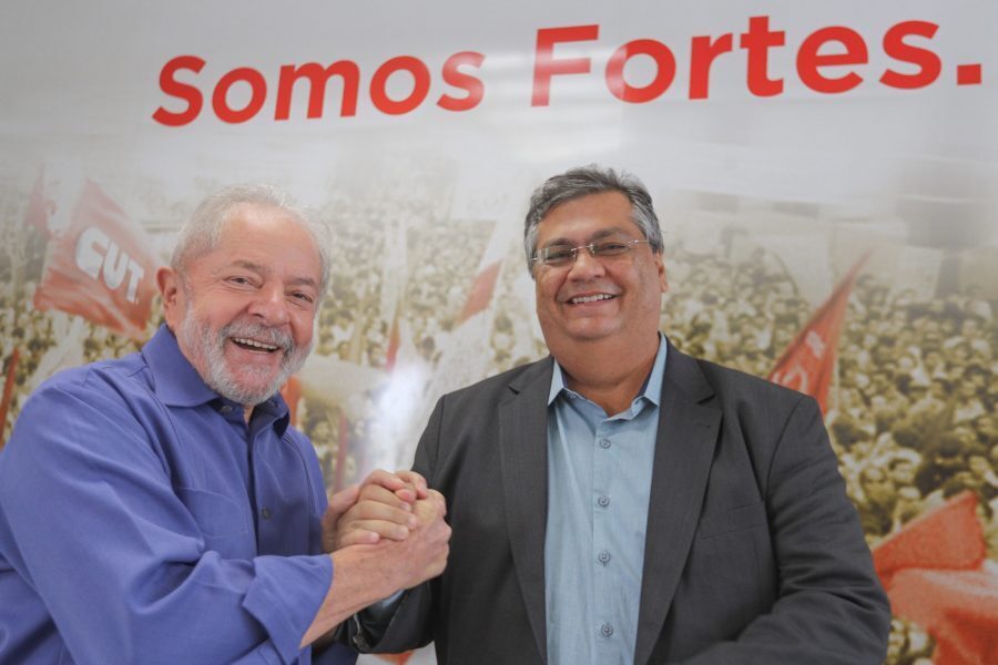 Foto de Lula e Flávio Dino dando as mãos. Atrás, a inscrição no cartaz: "Somos Fortes"