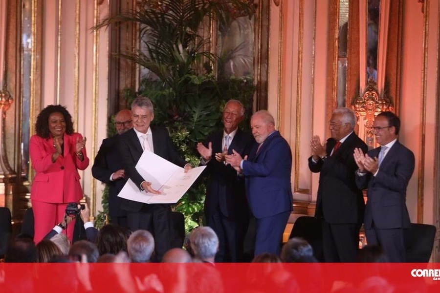 Cerimônia de entrega do Prêmio Camões para Chico Buarque, que exibe seu diploma ao público. Ao fundo, a ministra da Cultura Margarete Menezes, o presidente de Portugal e o presidente Lula aplaudem
