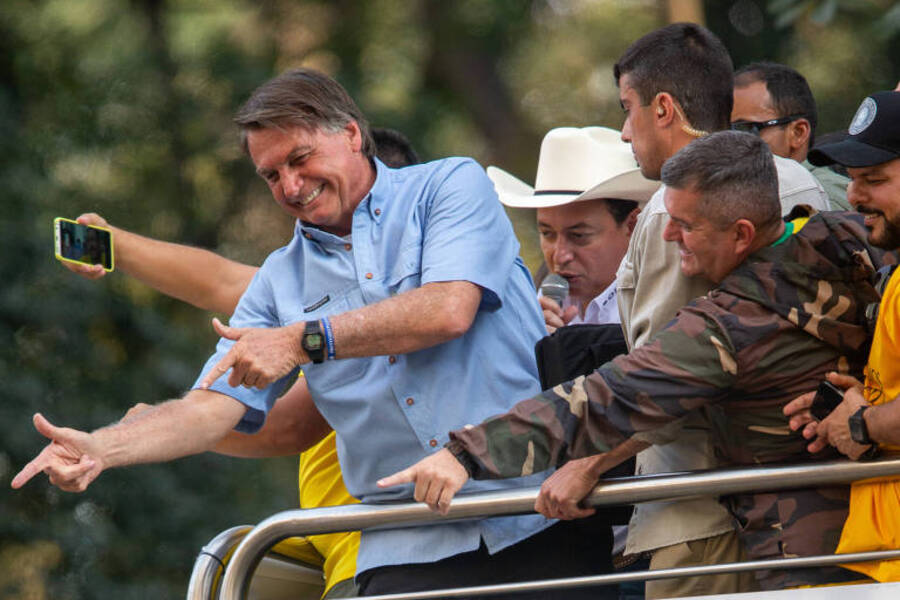 Jair Bolsonaro faz arminha com as duas mão e, de cima do caminhão do som, aponta para alguém do público