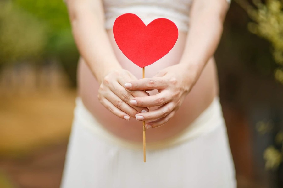 Foto de uma mulher grávida que porta um ornamento em forma de coração em frente à sua barriga