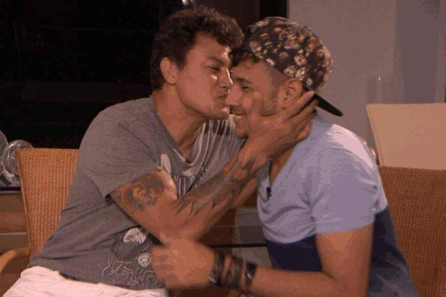 Acelino Popó e seu filho Juan Freitas estão sentados. Acelino, à esquerda. Ele, sorrindo, prepara-se para beijar seu filho no rosto.