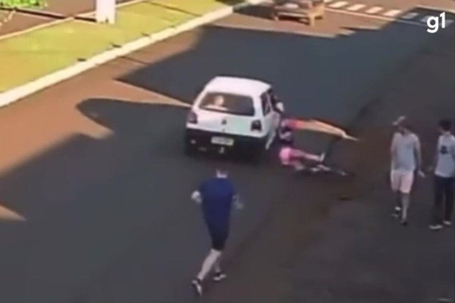Mulher está caída bem ao lado de um carro, cujo passageiro acabou de lhe agredir com um tapa nas nádegas