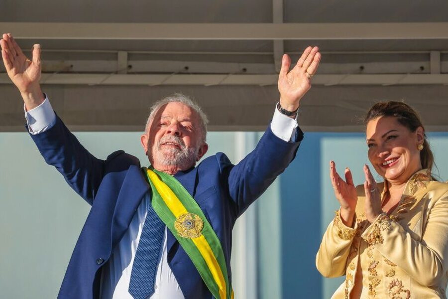 Lula, ao lado de Janja no parlatório, ergue os dois braços para o céu, saudando o grande público presente.