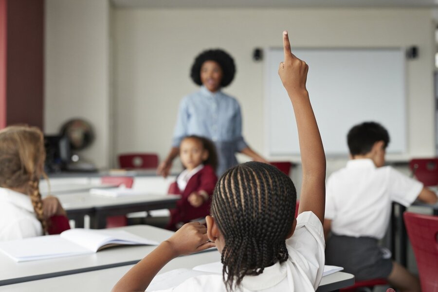 Professora em sala de aula vê aluno levantando a mão para falar