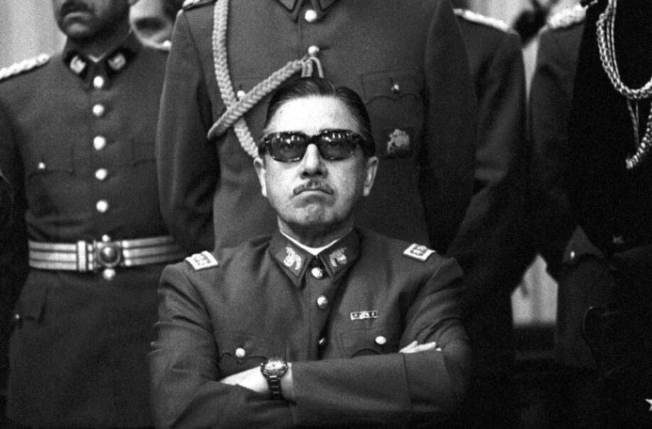 Foto do ditador Pinochet sentado de braços cruzados e cara de mau