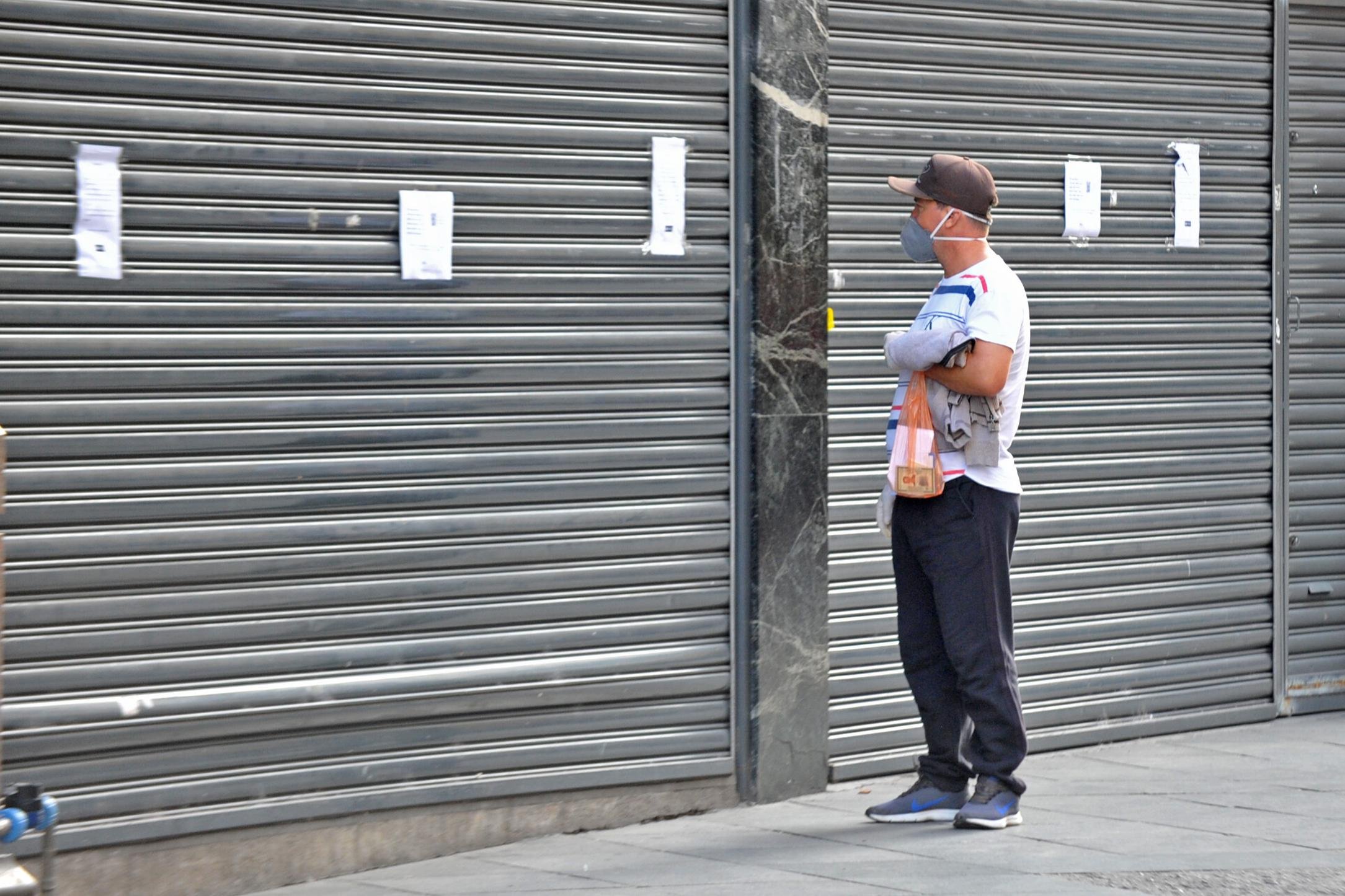 Cidadão observa cartaz ilegível diante de uma loja com as portas fechadas
