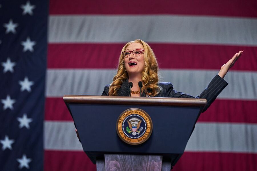 A atriz Maryl Streep, que interpreta a presidente dos EUA, está na tribuna falando. Ao fundo a bandeira dos EUA.