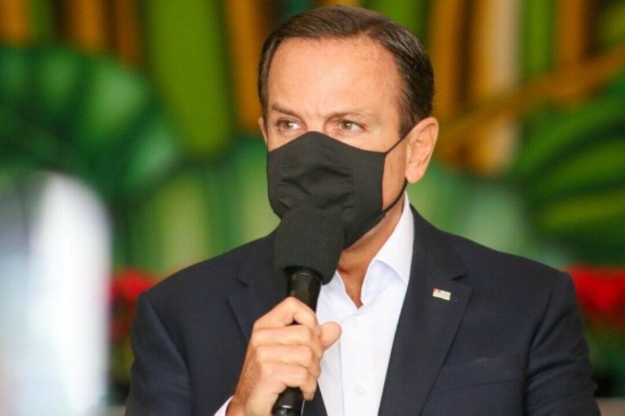 Foto do governador João Dória, com máscara, segurando o microfone