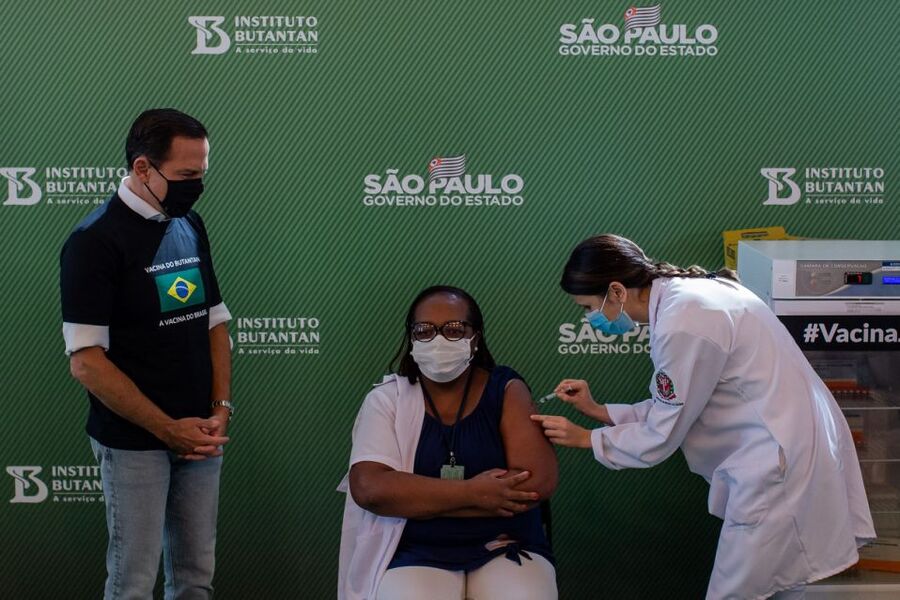 O governador João Doria de pé observa a enfermeira Mônica Calazans sendo vacinada contra a Covid-19