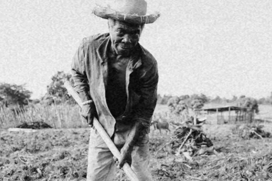 Homem negro trabalhando no campo, com enxada nas mãos.