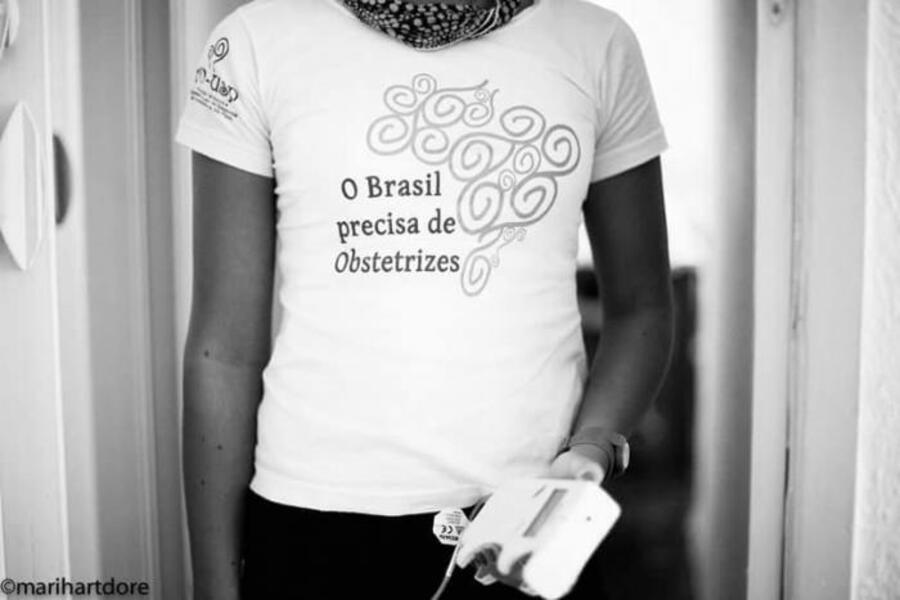 Foto em close de uma mulher vestindo uma camiseta com a inscrição "O Brasil precisa de Obstetrizes".