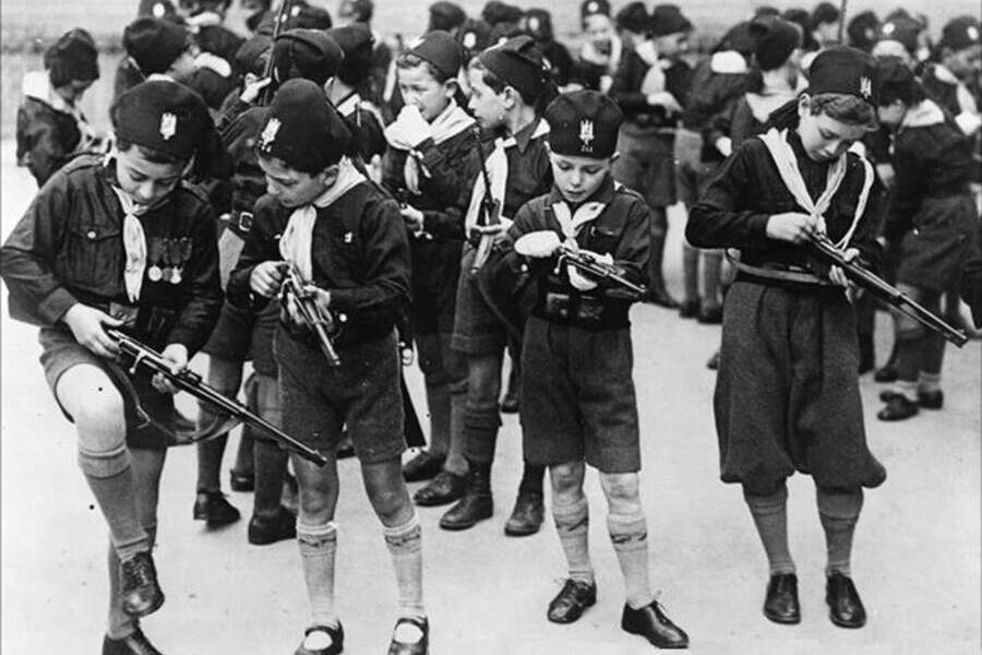 Crianças fardadas carregam rifles e metralhadoras