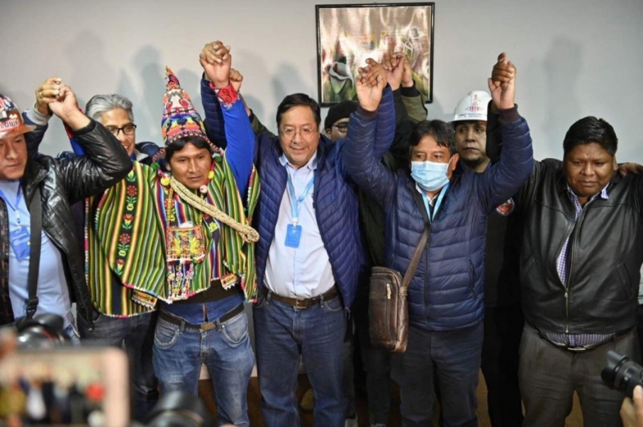 Um grupo de políticos do MAS com os braços erguidos e com mãos dadas comemoram a vitória de Arce, que está ao centro da foto