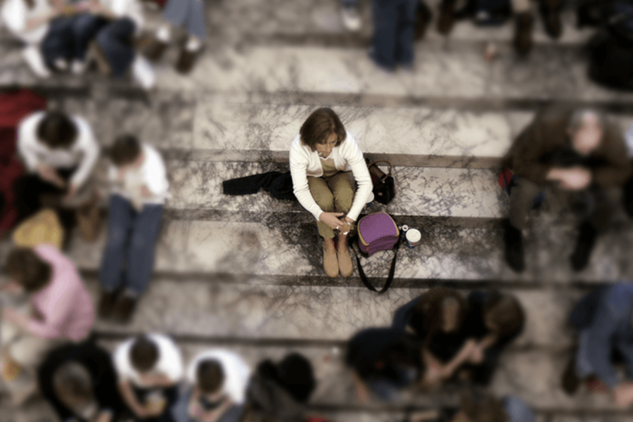 Imagem vista de cima de uma mulher sentada numa escadaria isolada da multidão que está à sua volta
