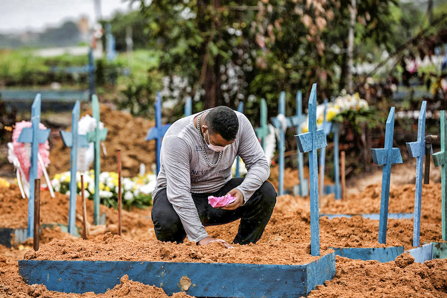 Foto de Homem agachado colocando flores em um dos milhares de túmulos de cemitério de campo aberto