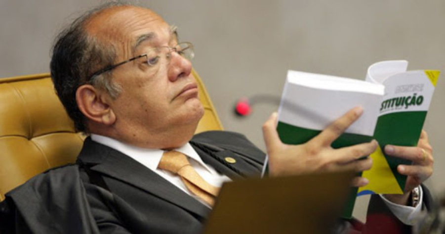Gilmar Mendes sentado lendo a Constituição