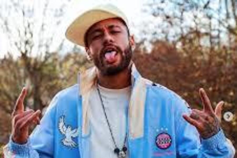 Jogador Neymar de boné e agasalho mostra a língua para o fotógrafo