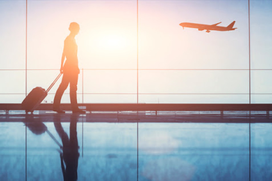 Um estudante dirige-se ao local de embarque no aeroporto. Pela janela, um avião que acaba de levantar vôo.