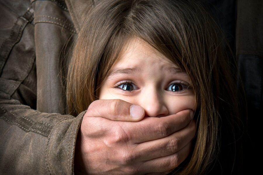Foto de uma mão masculina tapando a boca de uma menina que está apavorada