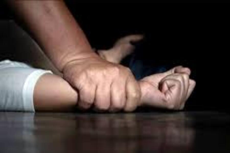 Mão masculina e de adulto segura firmemente o braço de uma criança contra ao chão simulando que pode estar havendo um estupro