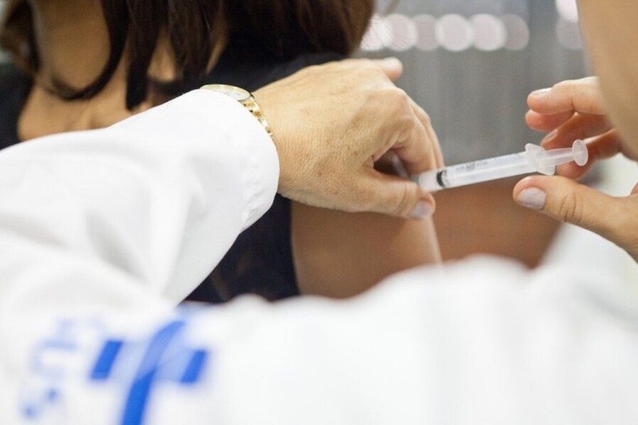 Enfermeiro com o jaleco do SUS aplica vacina contra HPV no braço de uma mulher