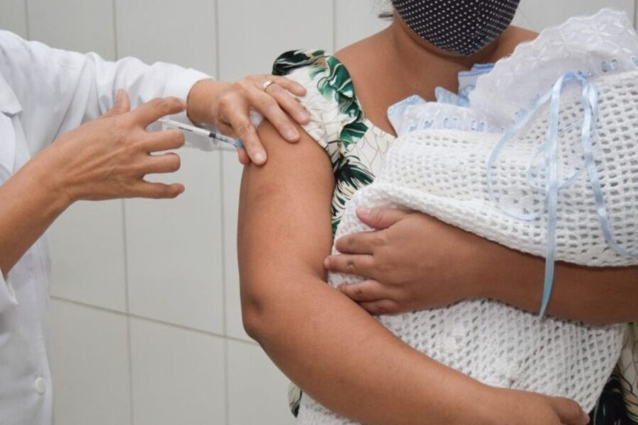 Mulher com recém-nascido no colo está tomando a vacina contra covid-19