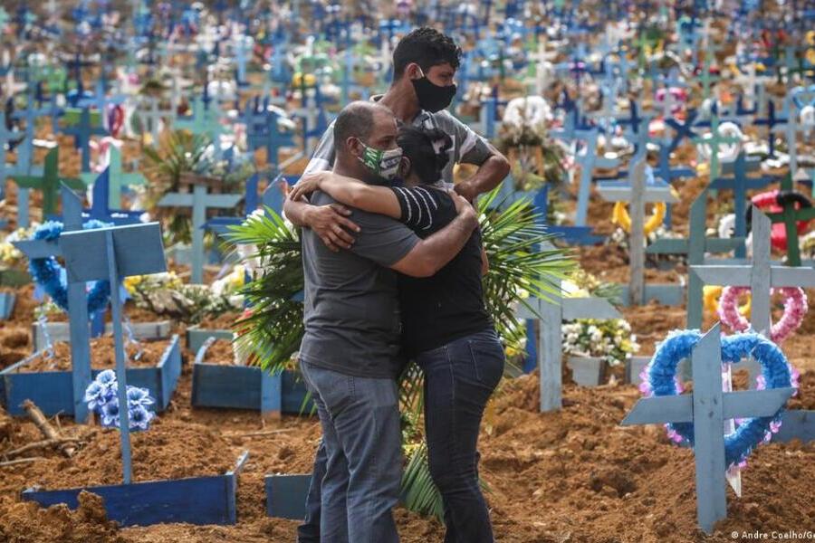 Um homem e duas crianças se abraçam no meio do cemitério em que acabaram de enterrar um ente querido