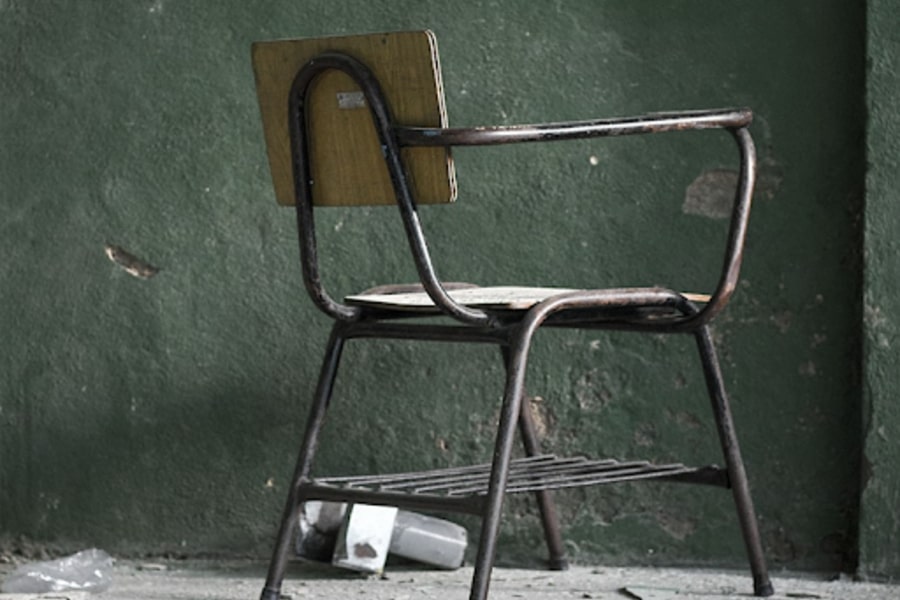 Uma cadeira escolar vazia no canto de uma sala mal cuidada.