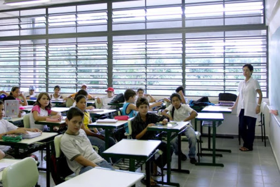 Foto de sala de aula com alunos e professora. Todos sem máscara.
