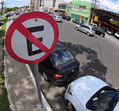 Foto de dois veículos estacionados em baixo de uma placa de "proibido estacionar"
