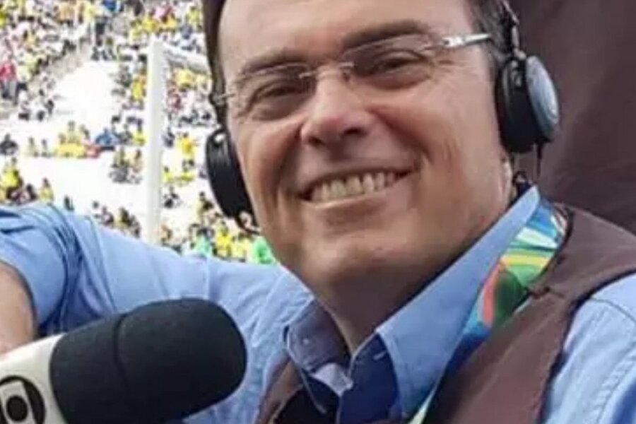 Foto de Tino Marcos posando para as lentes da câmara durante partida de futebol. Estão com fone de ouvido e segurando seu microfone com a logo da Globo
