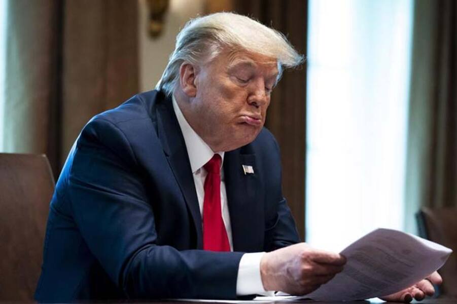 foto de Donald Trump sentado em sua mesa na Casa Branca lendo papeis e fazendo biquinho