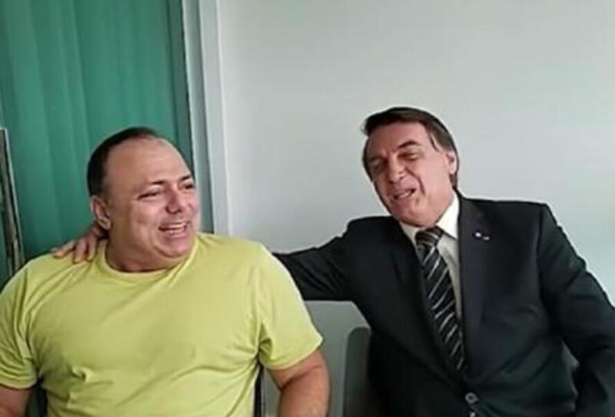 Ministro Pazuello e Jair Bolsonaro riem sentados e pousando para a câmera. Bolsonaro está com a mão sobre o ombro do ministro