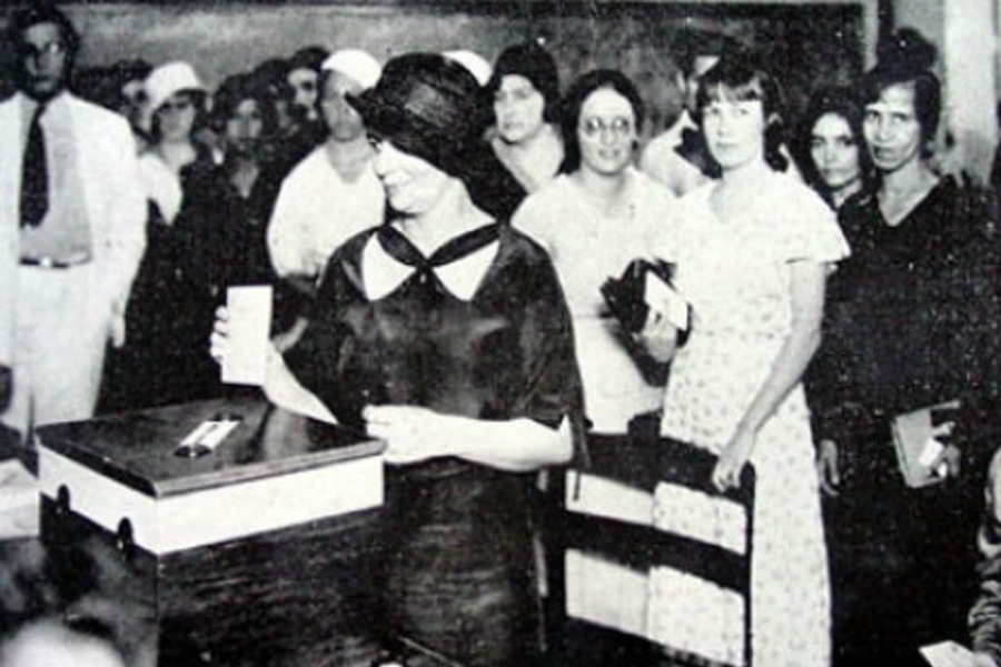 Foto antiga, provavelmente, de 1932, na primeira eleição que mulheres puderam votar. Na Foto, uma mulher, acompanhadas por várias outras, deposita seu voto na urna